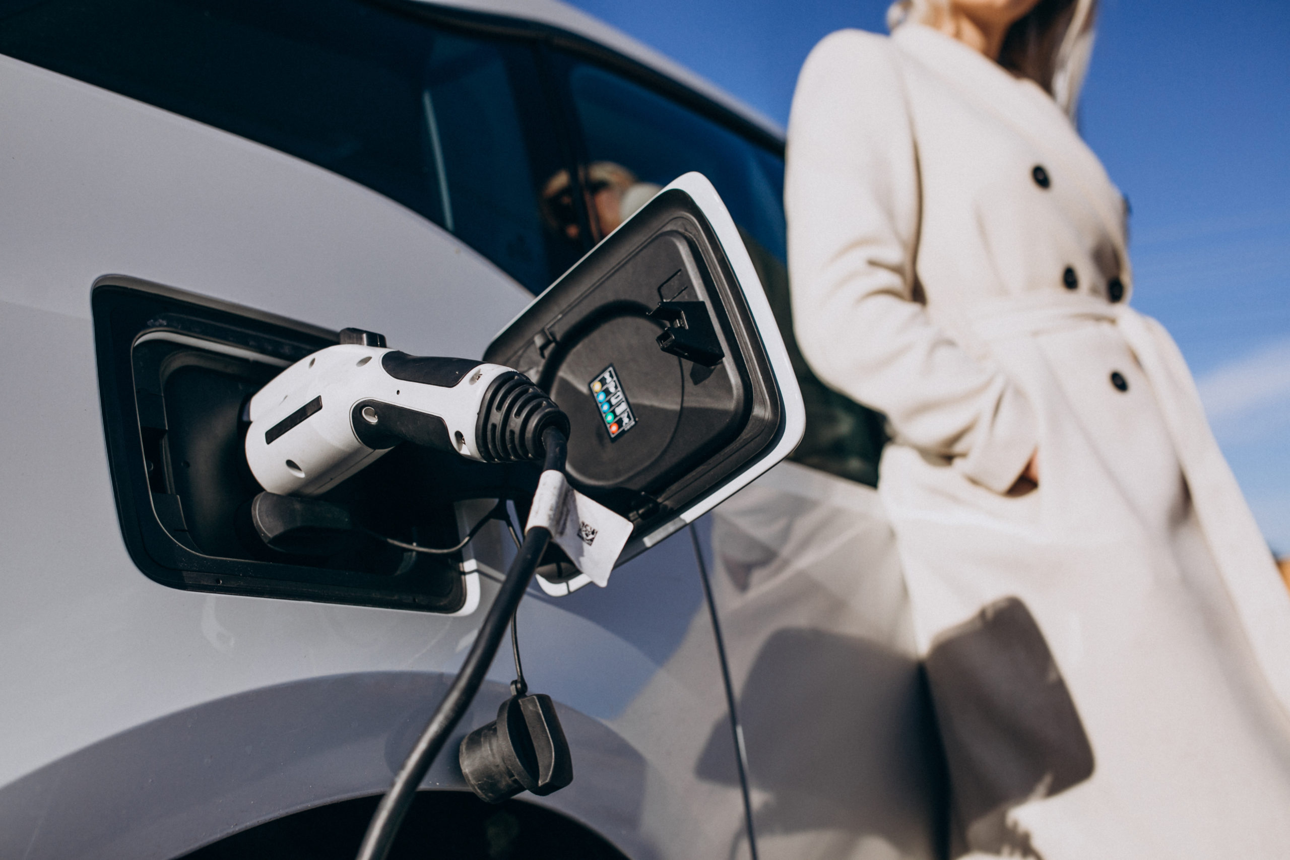A woman leans against an electric vehicle as it charges