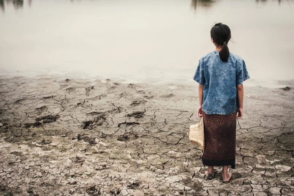 water scarcity: A girl stands on dry, cracked ground facing away from the camera.