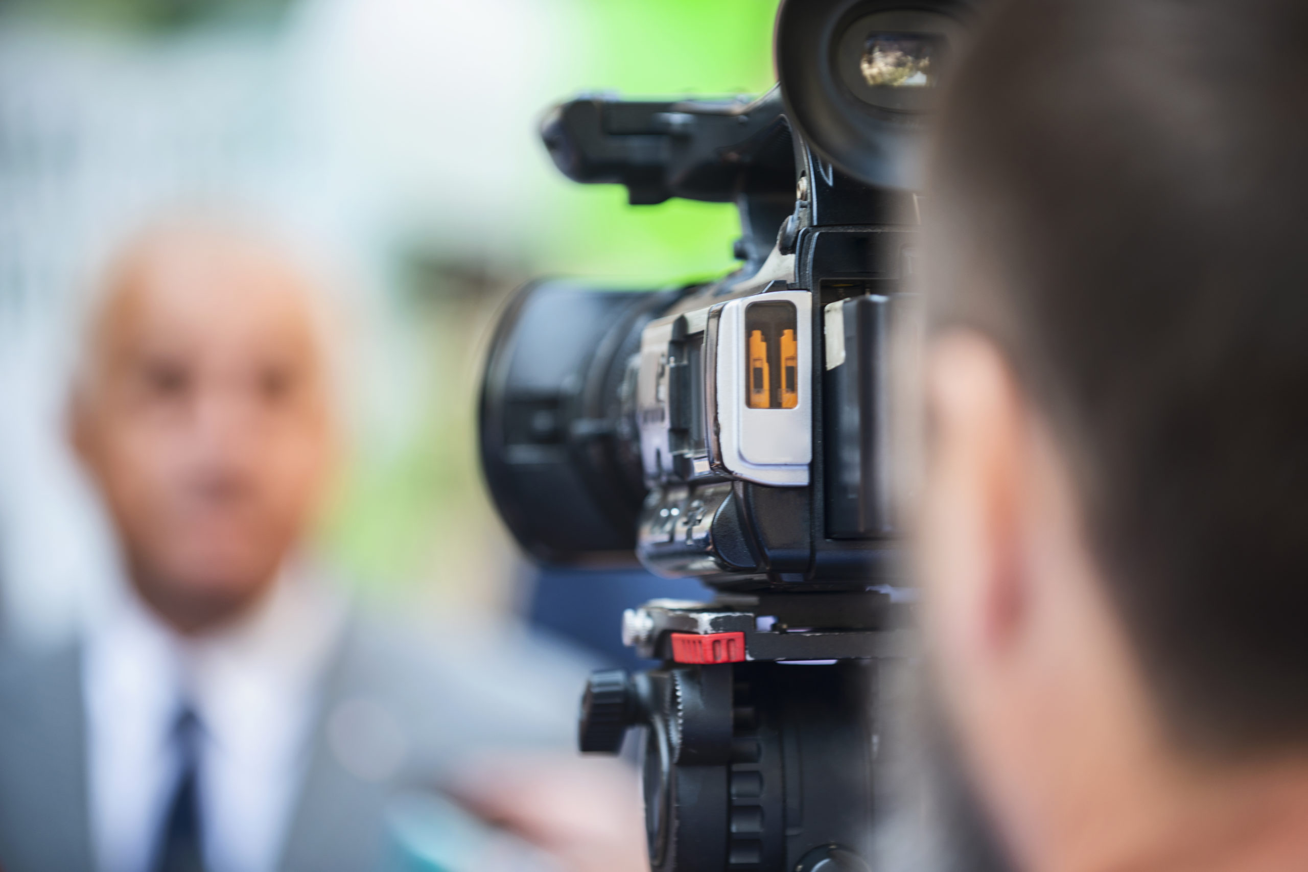 Media Relations: Camera operator working at a press conference outdoors. Journalists interviewing formal dressed politician or businessman at a media event.