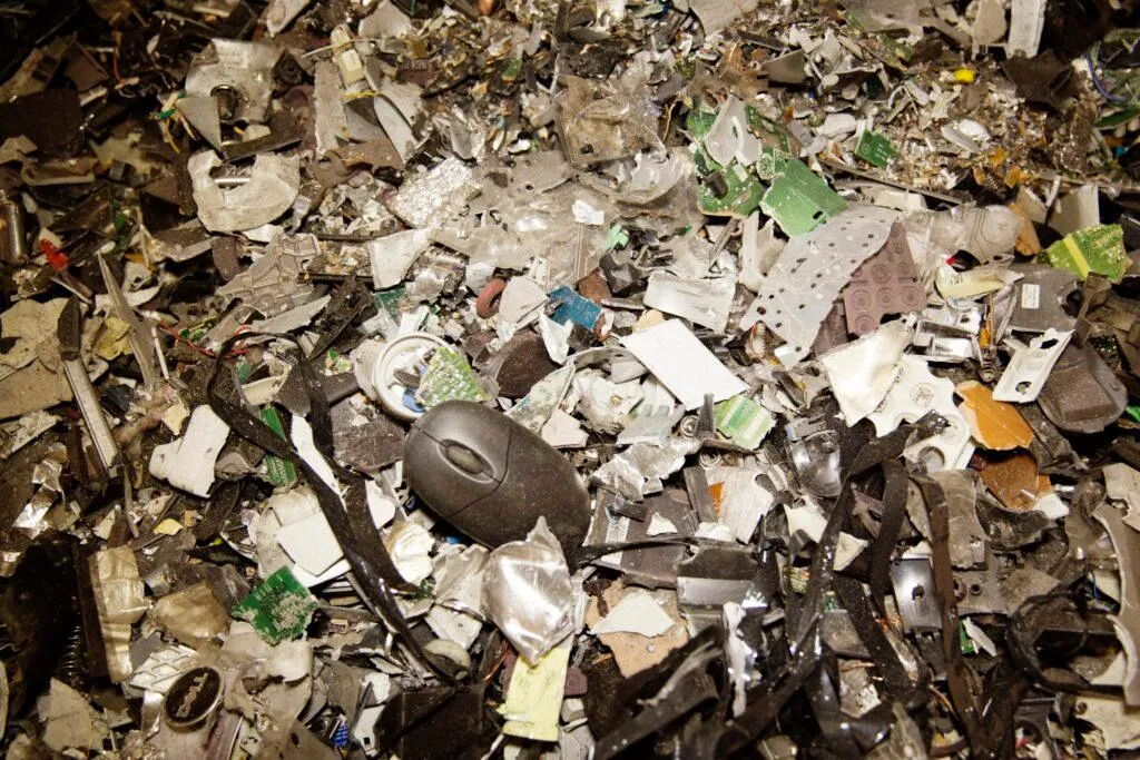 A discarded mouse sits on top of a pile of trash and electronic components, illustrating the growing problem of electronic waste.