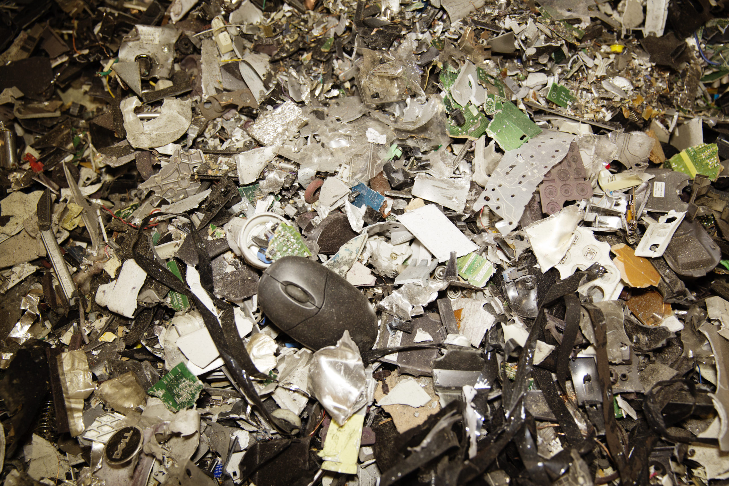 A discarded mouse sits on top of a pile of trash and electronic components, illustrating the growing problem of electronic waste.
