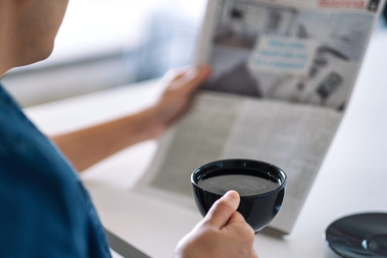 Closeup image of a man reading newspaper and drinking coffee in the morning