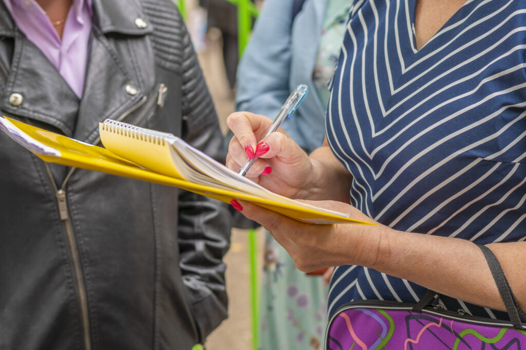 Stakeholder Engagement: Woman with yellow folder and notebook stands among group of people to take a survey.