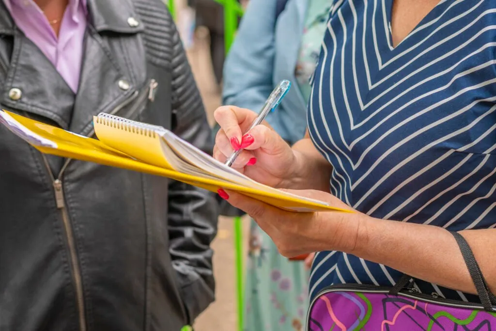 Stakeholder Engagement: Woman with yellow folder and notebook stands among group of people to take a survey.