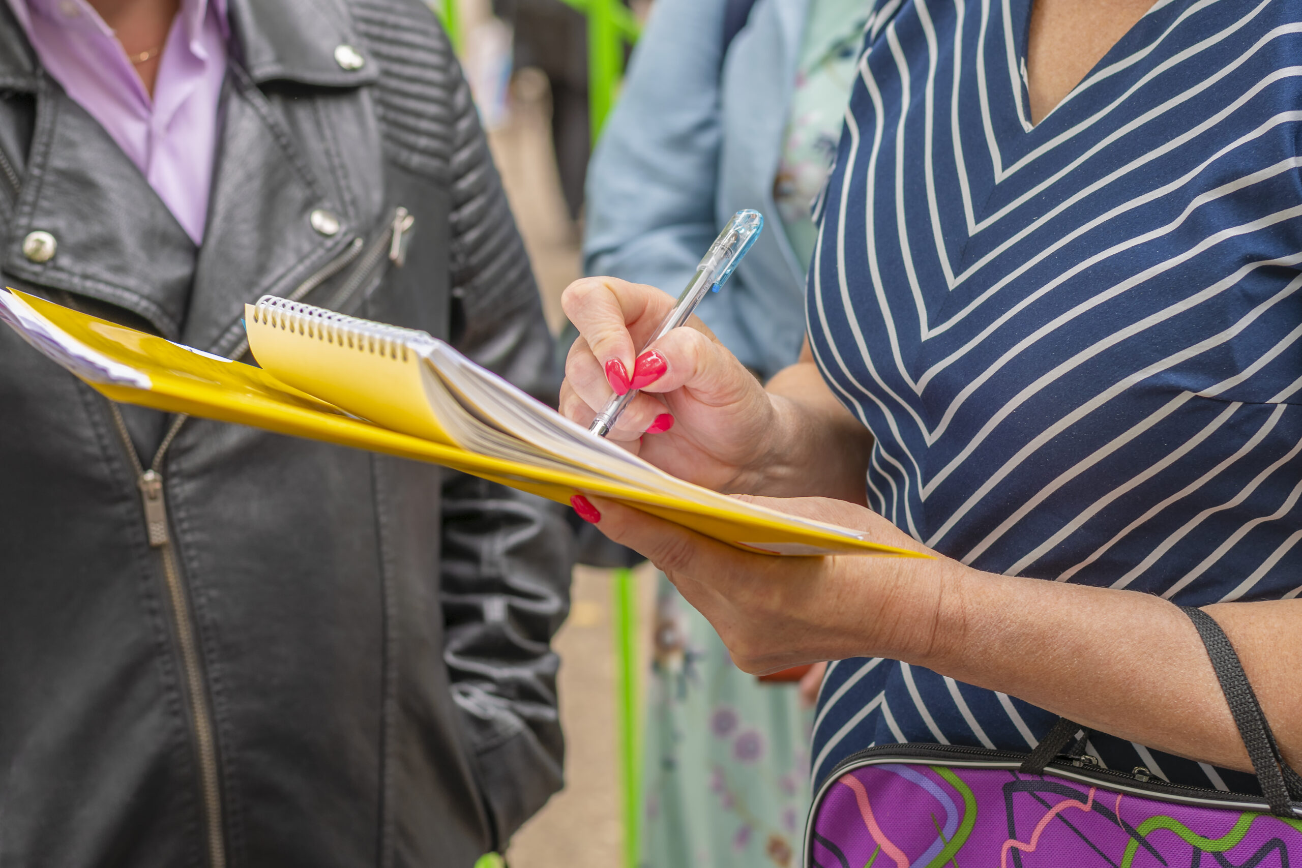 Stakeholder Engagement: Woman with yellow folder and notebook stands among group of people to take a survey.