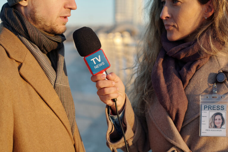 media relations: Cropped shot of young man in beige coat answering question of female journalist of TV channel during outdoor interview