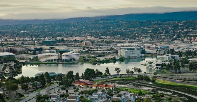 Aerial view of Silicon Valley offices and neighborhoods surrounding a waterfront under a cloudy sky.