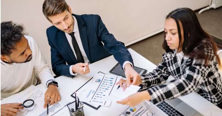 Three business professionals reviewing charts and data together at a conference table.