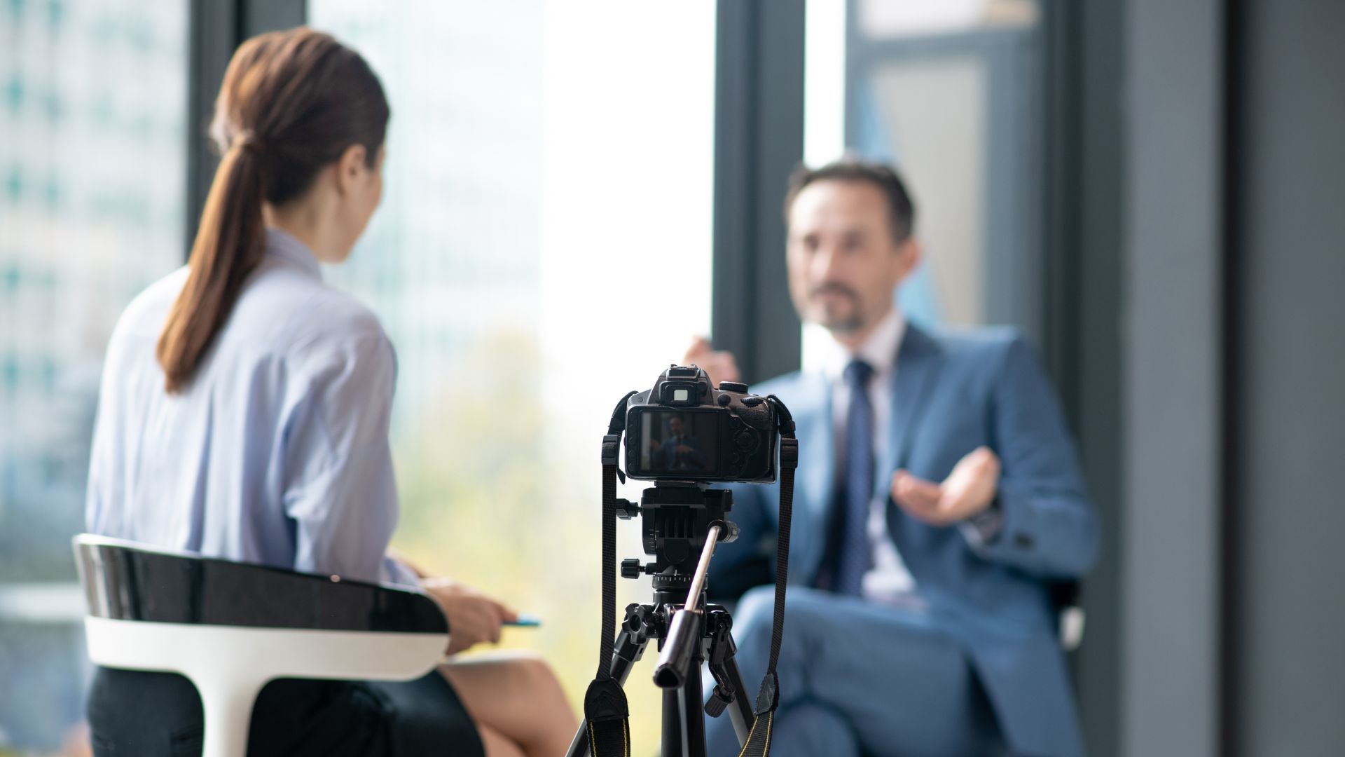 Media training is illustrated with a photo depicting a woman interviews a man in a professional setting while a camera on a tripod records their conversation. The woman has her back to the camera, and the man, wearing a suit, is speaking with hand gestures. The background shows large windows with a blurred cityscape.