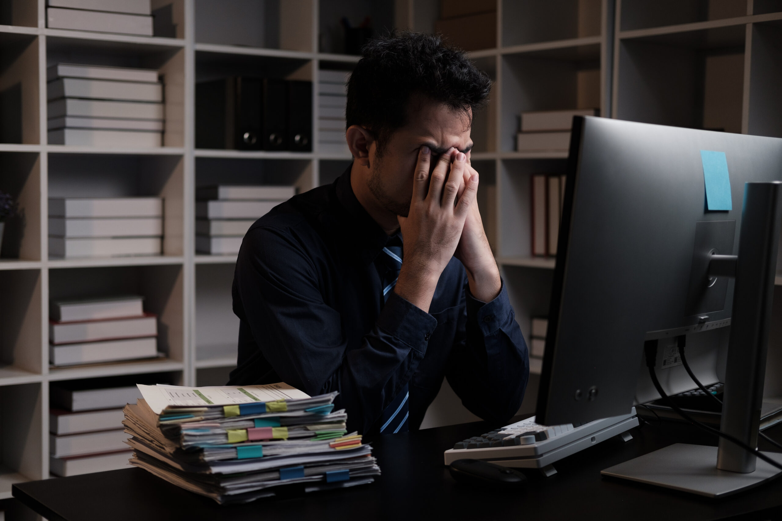 Information Overload: Stressed tired young man feeling headache while working overtime at night in his office